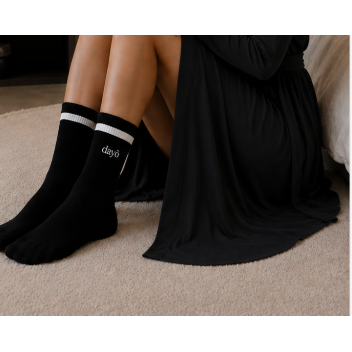 Black crew socks with white stripes and the brand name 'dayō' printed in white on the side, worn by a person sitting on a beige carpet.